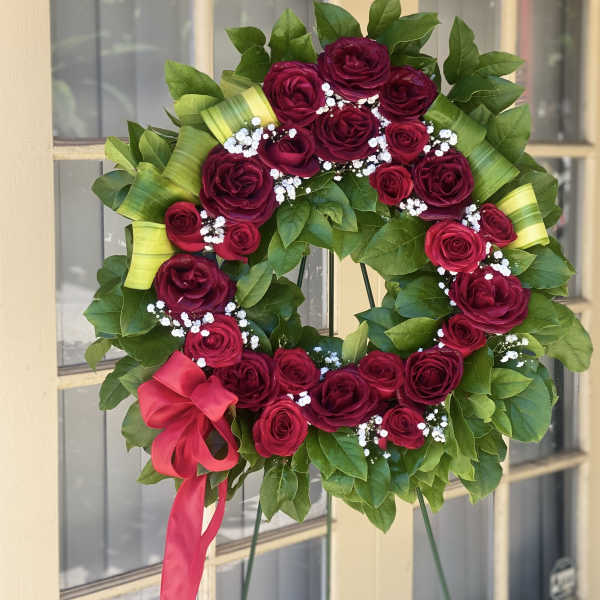 Circular wreath of red roses with white baby's breath and a pink ribbon