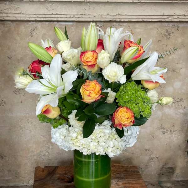 Bouquet of white lilies, roses, and hydrangeas in a green glass vase
