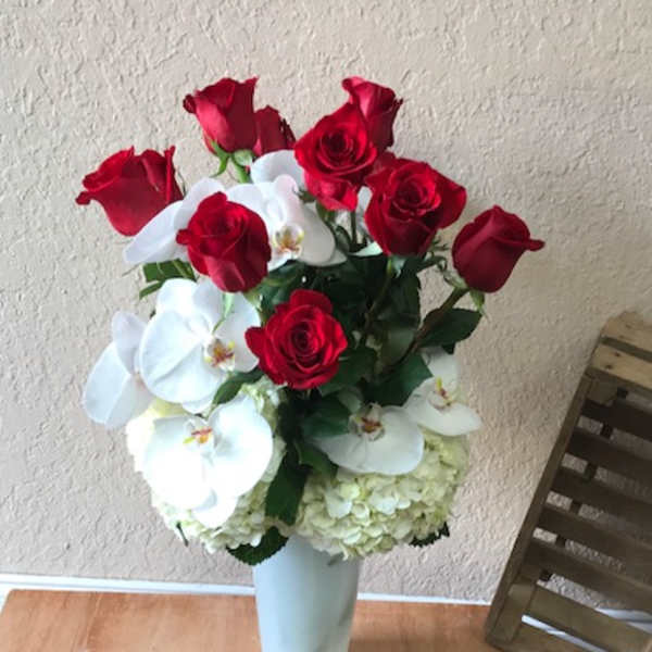 Red roses and white orchids arranged in a tall white vase
