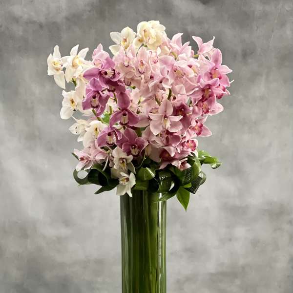 Tall cylinder vase of pink and white orchids with wrapped green stems and stones at the base