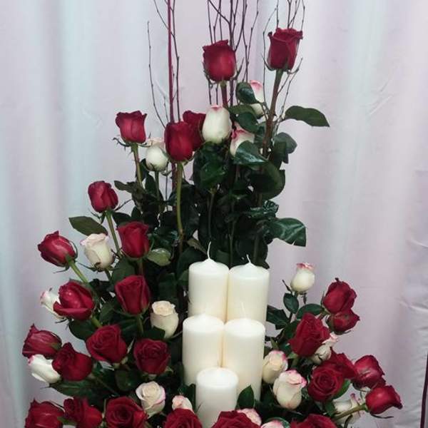Red and white roses arranged around white pillar candles on a glass table