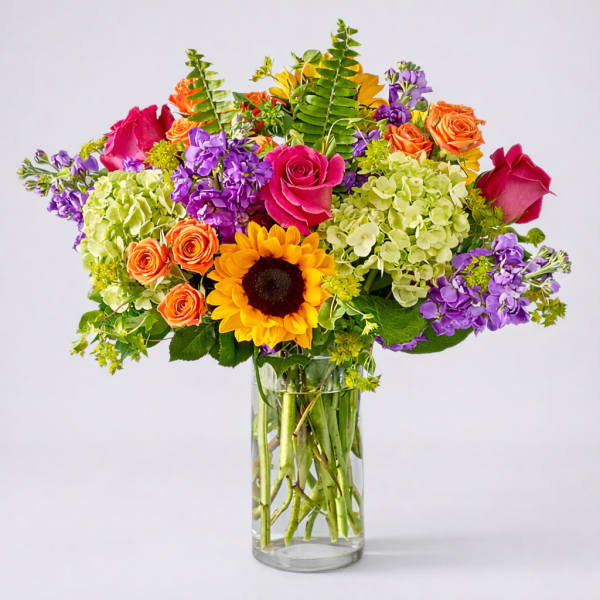 Colorful bouquet of roses, hydrangeas, and a sunflower in a glass vase