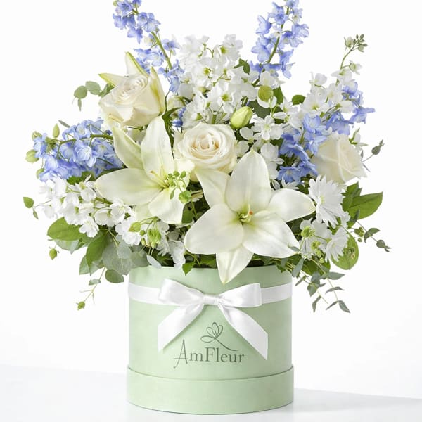White lilies and roses with blue flowers in a mint green hat box