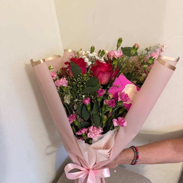 Pink bouquet with red roses and carnations wrapped in blush paper