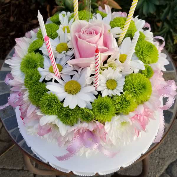 Round floral cake with pink rose, daisies, and striped candles