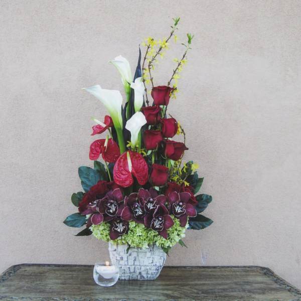 Tall floral arrangement with red roses, white calla lilies, and orchids in a white vase