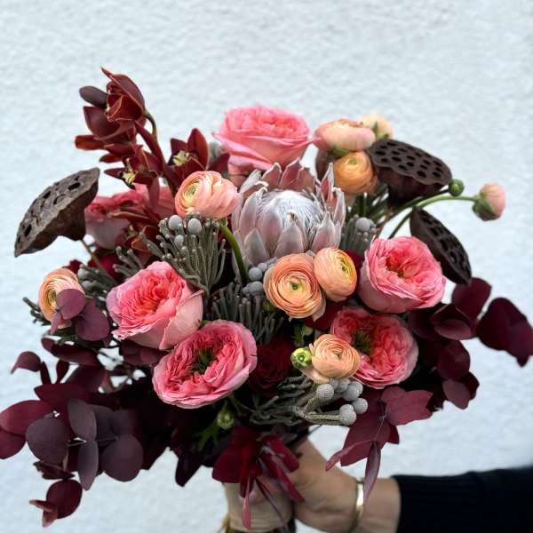 Handheld bouquet of pink and burgundy flowers with dark foliage