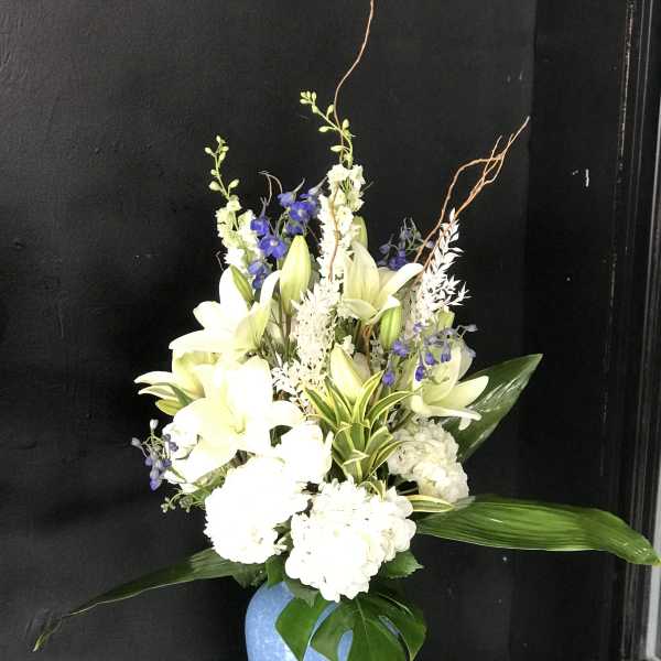 White lilies and blue flowers arranged in a blue vase