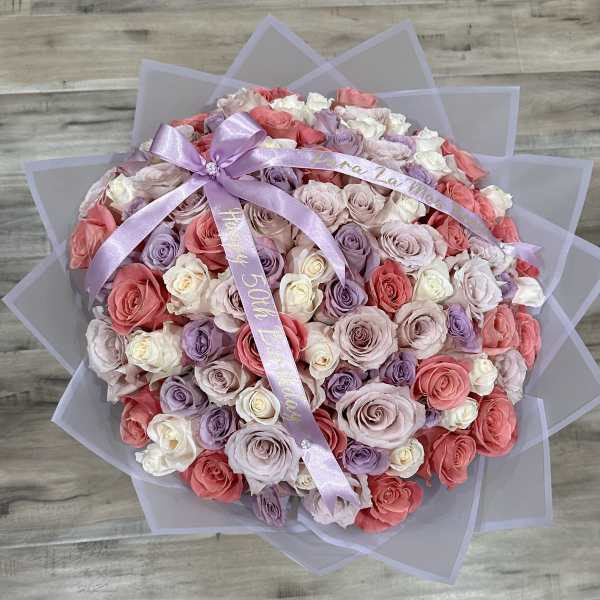 Round bouquet of pink, lavender, and white roses with a lavender ribbon