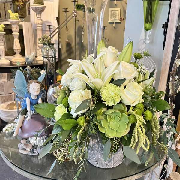 White roses and lilies in a silver container with green succulents