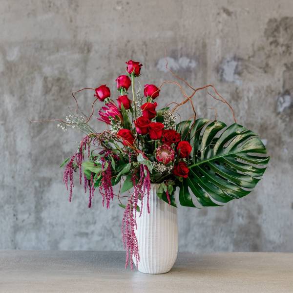 Red rose arrangement in a white vase with tropical leaves