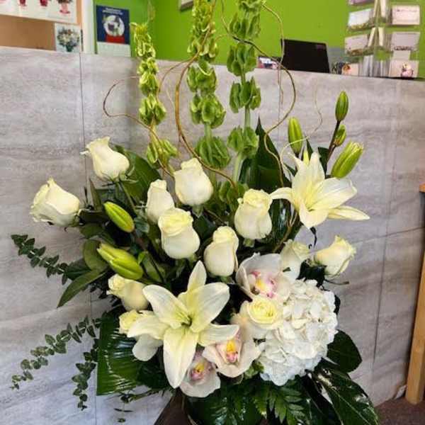 White lilies and roses arranged in a tall vase with green accents