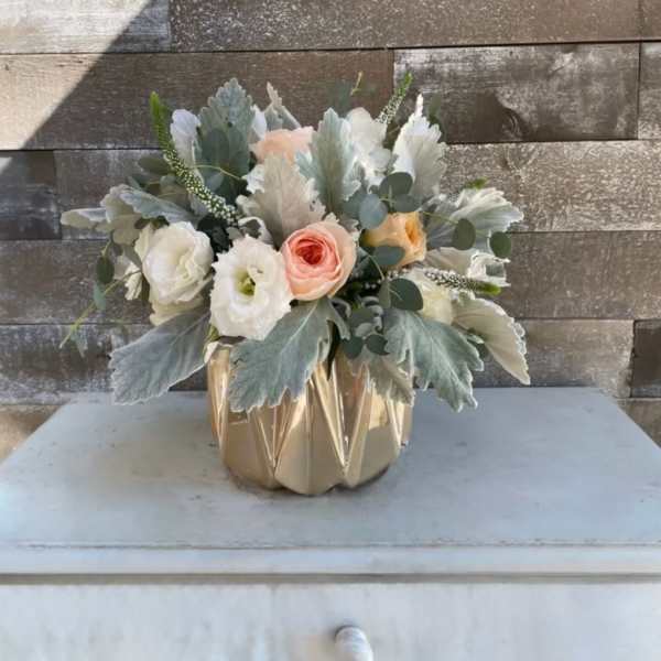 Compact bouquet of pastel roses and white blooms in a gold vase