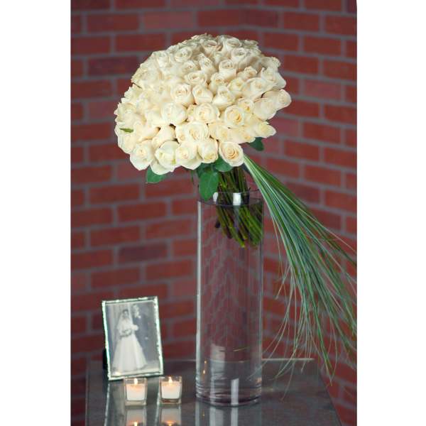 Cream rose bouquet in a tall glass vase with a long grass accent.