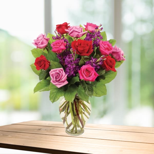 Bouquet of red, pink, and purple roses in a clear glass vase