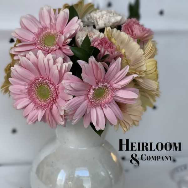 Pink gerbera daisies and carnations arranged in a white vase