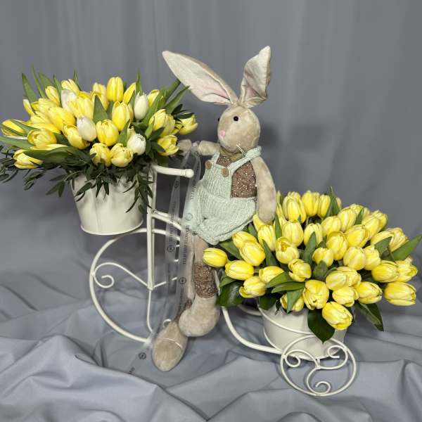 Two yellow tulip arrangements in white buckets with a plush bunny between them