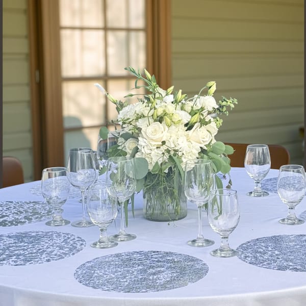 White floral centerpiece in a glass vase on a round table with wine glasses