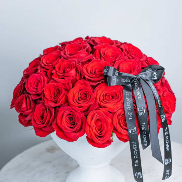 Round bouquet of red roses in a white vase with a black ribbon