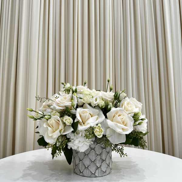 Low arrangement of ivory roses and white blooms in a textured gray vase on a round table