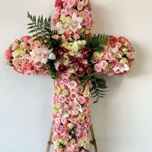 Large floral cross covered in pink roses and orchids on an easel