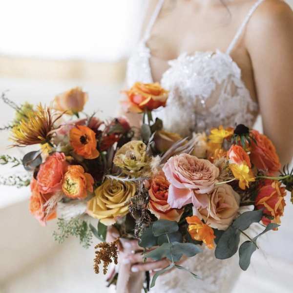 Bride holding a colorful bouquet of roses and orange blooms