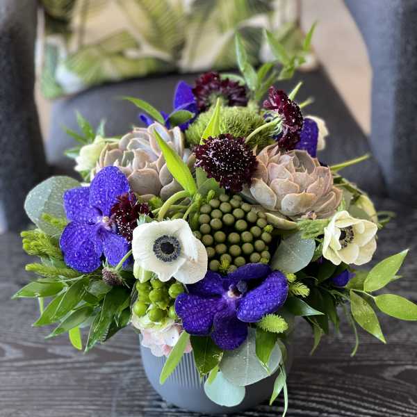 Mixed bouquet with purple orchids and pale succulents in a gray vase