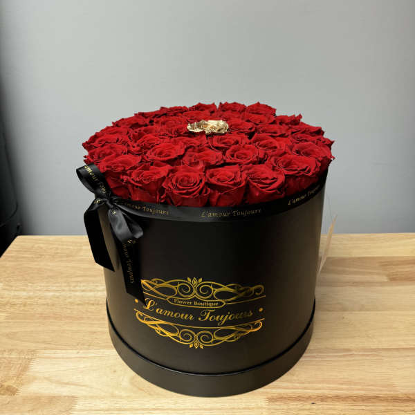 Round black hatbox filled with red roses and one gold rose on a wooden table