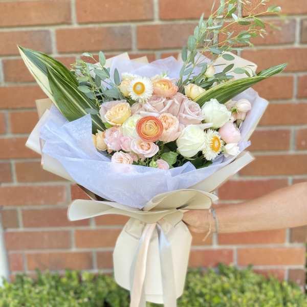 Hand-tied bouquet of pastel roses and white daisies wrapped in pale paper