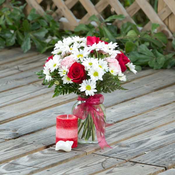 Bouquet of red roses and white daisies in a glass vase with a pink ribbon