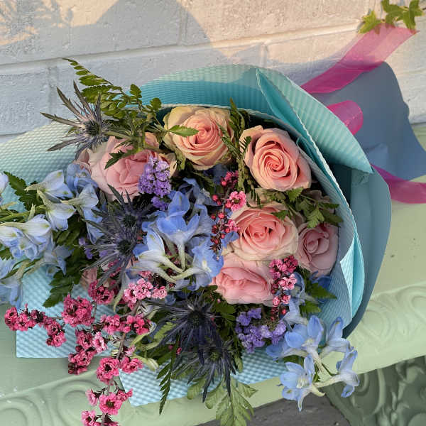 Bouquet of pink roses and blue flowers wrapped in turquoise paper