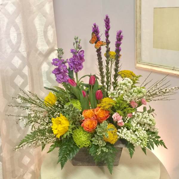 Mixed floral arrangement in a rectangular container with purple, yellow, orange, pink, and white blooms