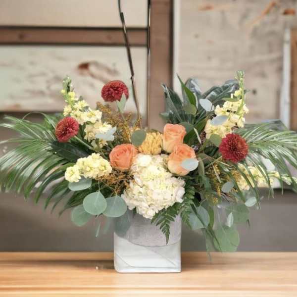 Mixed floral arrangement in a white square vase with peach and cream blooms