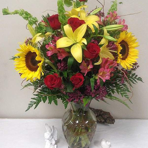 Mixed bouquet with red roses, yellow lilies, and sunflowers in a glass vase