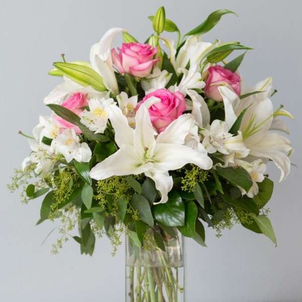 Pink roses and white lilies arranged in a tall glass vase
