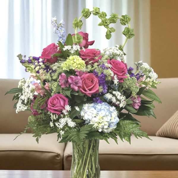 Mixed bouquet of pink roses, hydrangea, and purple flowers in a glass vase