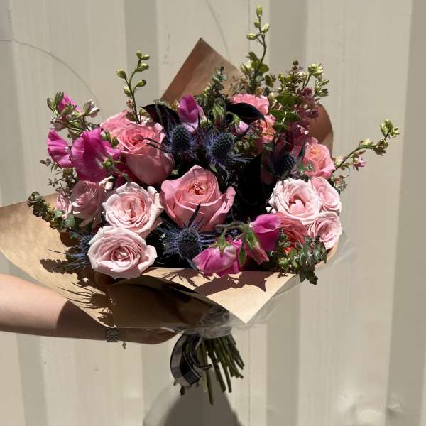 Hand-tied bouquet of pink roses and magenta blooms with dark blue thistles