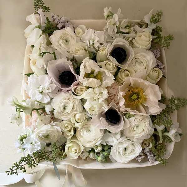 White floral bouquet with pale pink anemones and roses in a square wrap