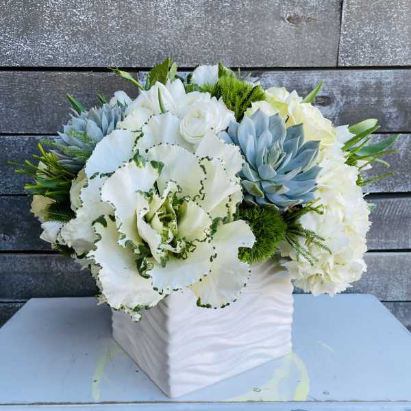 White floral arrangement in a square white vase with blue succulents