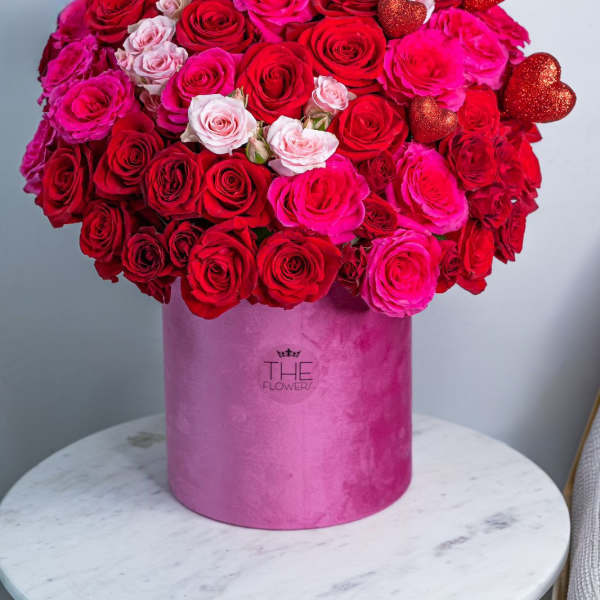 Large bouquet of red and pink roses in a pink hat box with heart picks