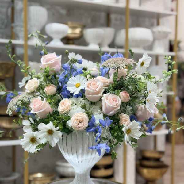 Pastel bouquet of pink roses, white daisies, and blue flowers in a white vase