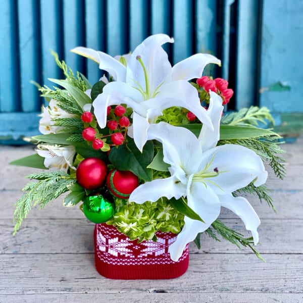 White lilies in a red knit container with holiday ornaments