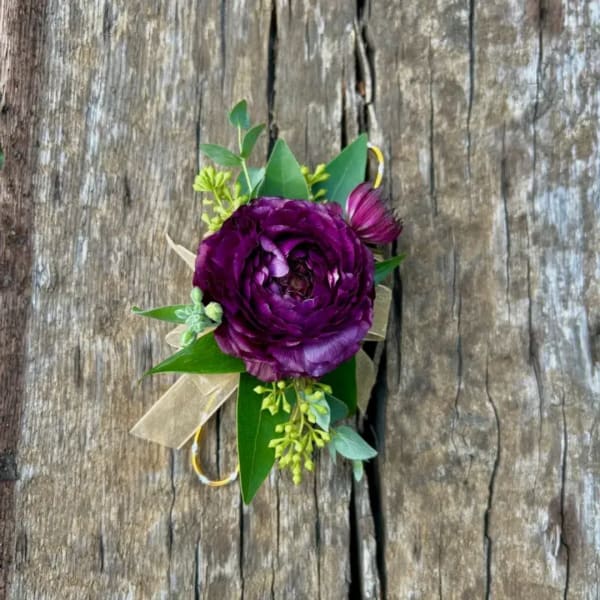 Purple flower boutonniere with green leaves and a ribbon on wood