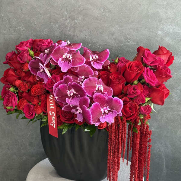 Red rose and purple orchid arrangement in a black vase