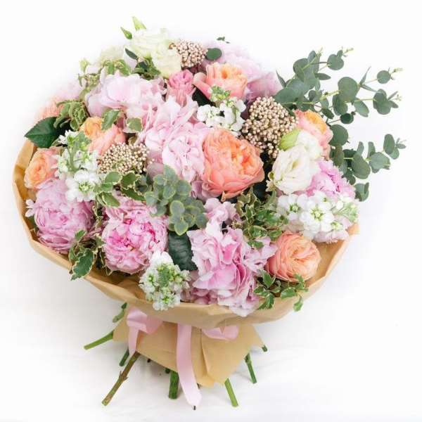 Bouquet of pink and peach flowers with eucalyptus wrapped in tan paper