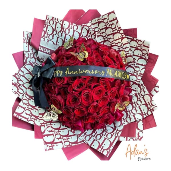 Red rose bouquet wrapped in pink Dior-pattern paper with a black ribbon