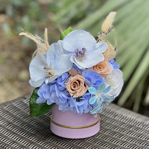 Blue hydrangeas and orchids arranged in a pink round box