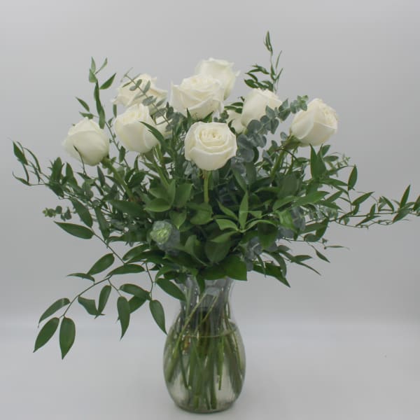 White roses in a clear glass vase with greenery