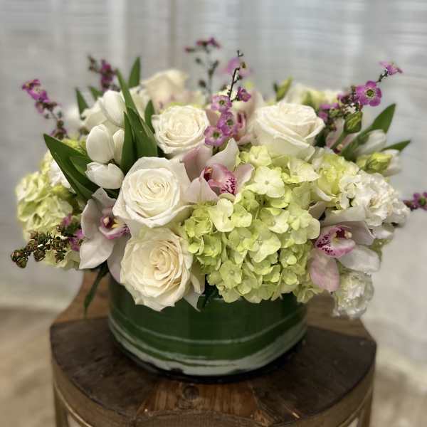 White roses and green hydrangeas in a green vase with pink orchid accents