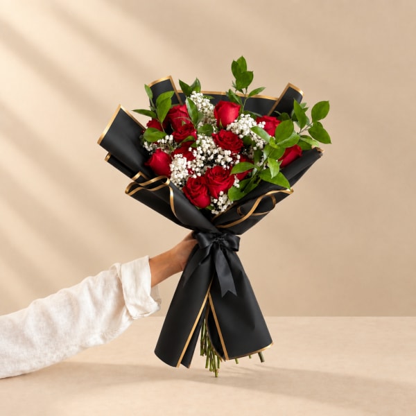 Handheld bouquet of red roses with white filler flowers in black wrap
